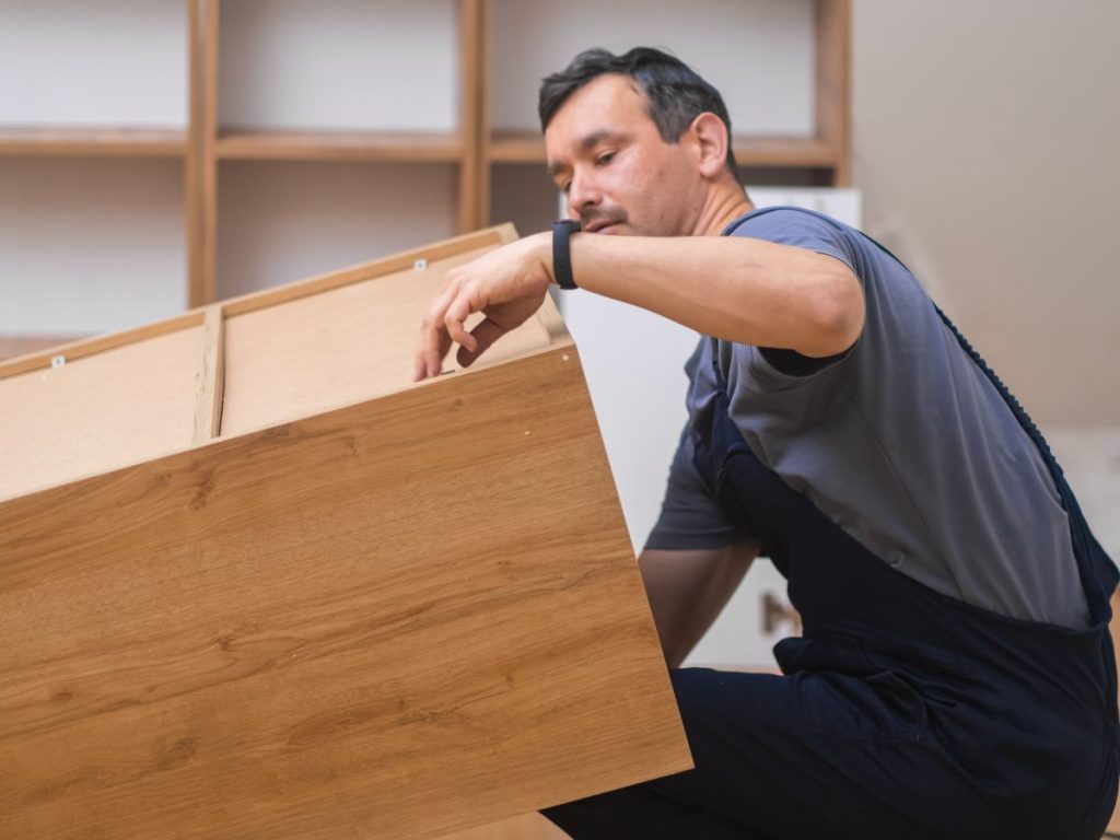 A person assembling a wooden drawer, focused on fitting its components, surrounded by a cozy interior workspace.