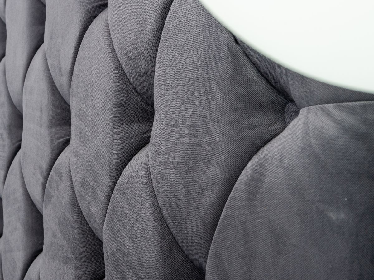 Close-up of a plush, tufted gray upholstery with soft fabric texture, showcasing deep, inviting indentations and smooth curves.