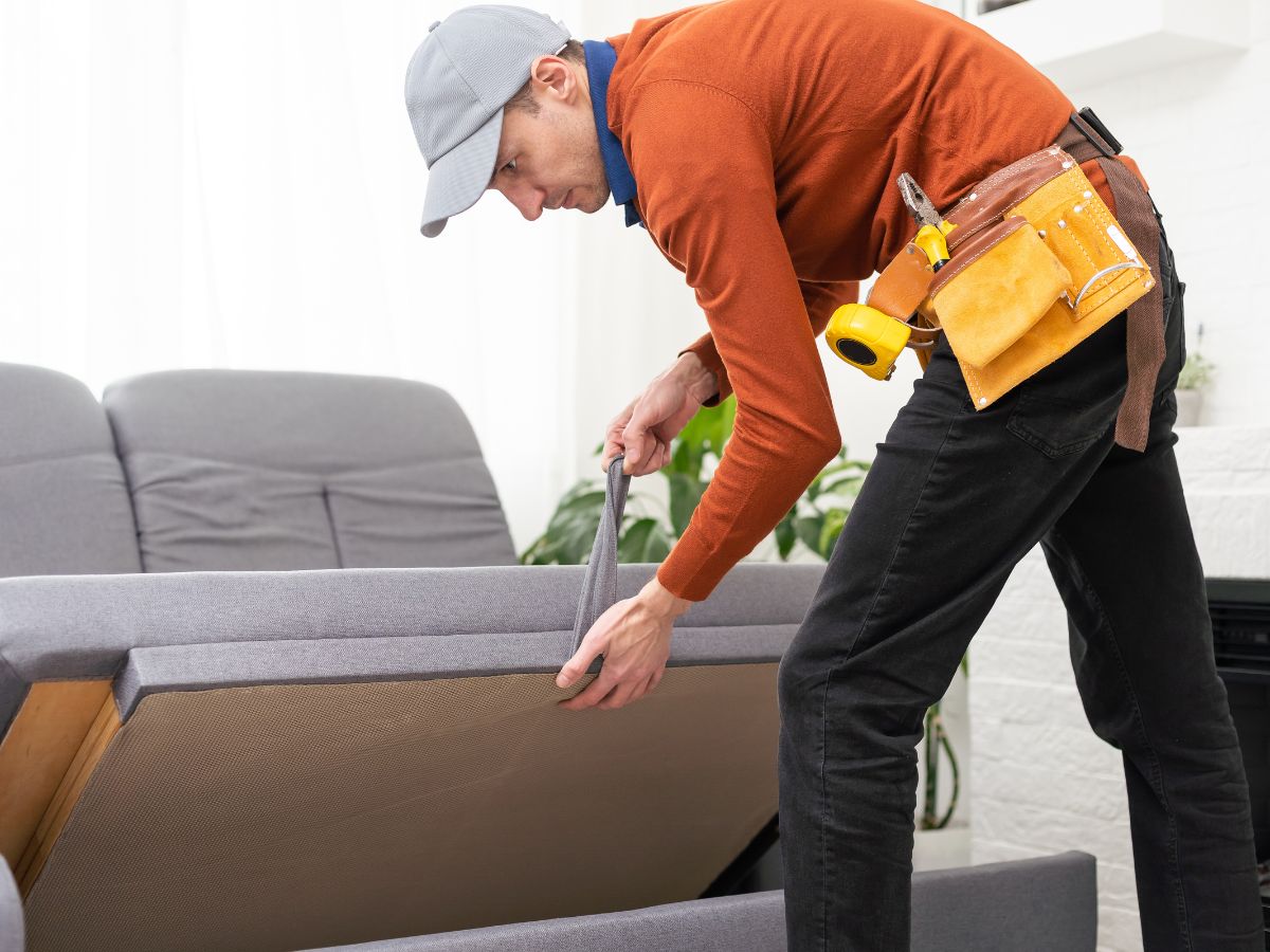A man working on assembling a couch in a bright living room filled with natural light.