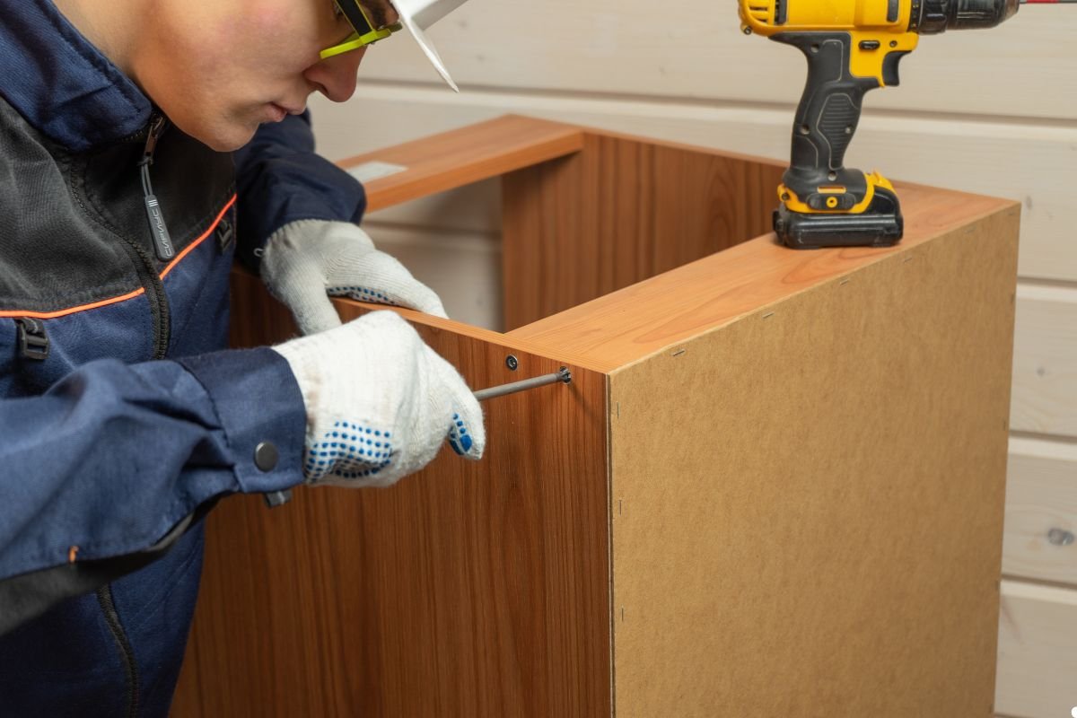 A man operates a drill to secure a wooden piece, demonstrating a home improvement task in a workshop setting.