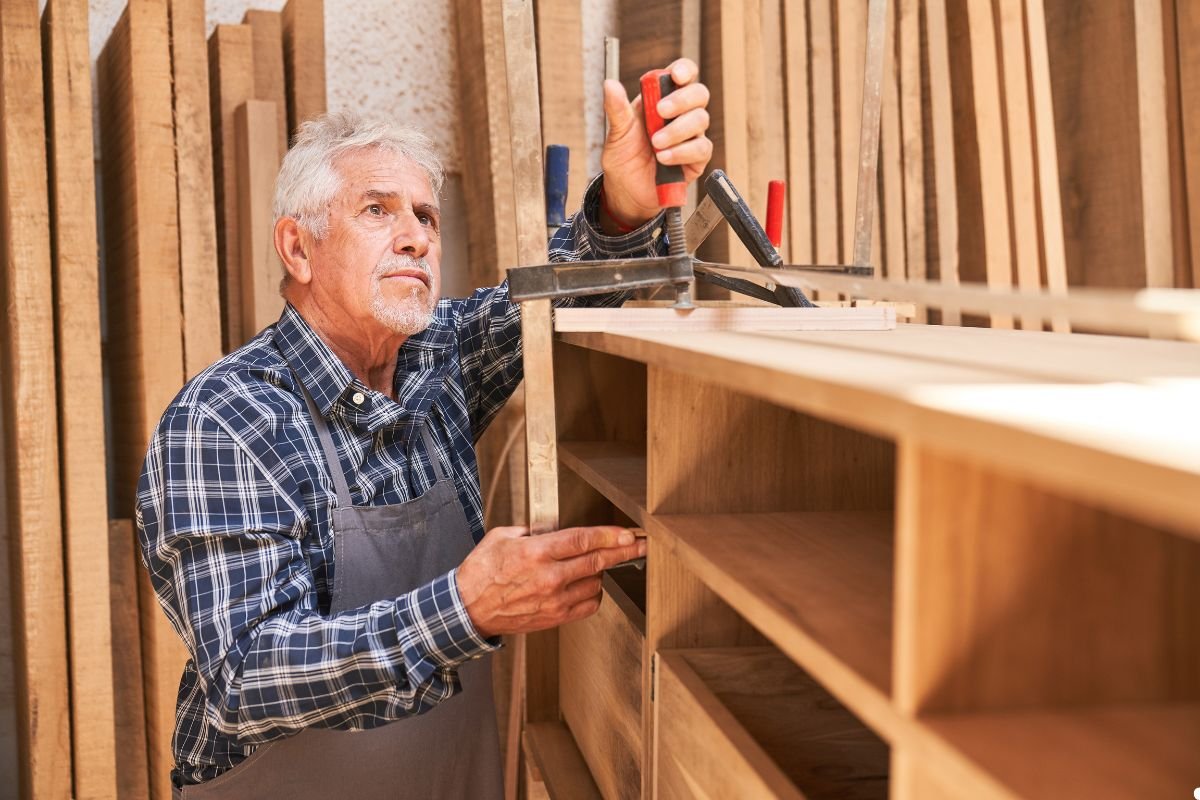 A man is focused on assembling a wooden shelf in a workshop, surrounded by tools and materials.