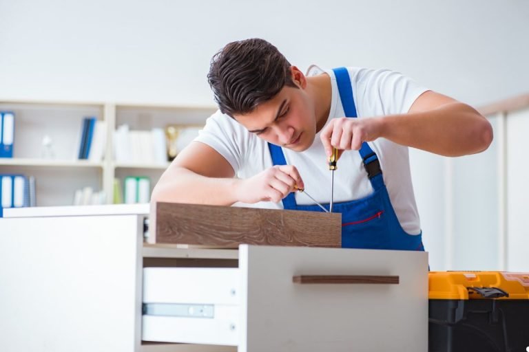 A man in an apron is diligently assembling a cabinet, surrounded by tools and wood materials in a workshop.