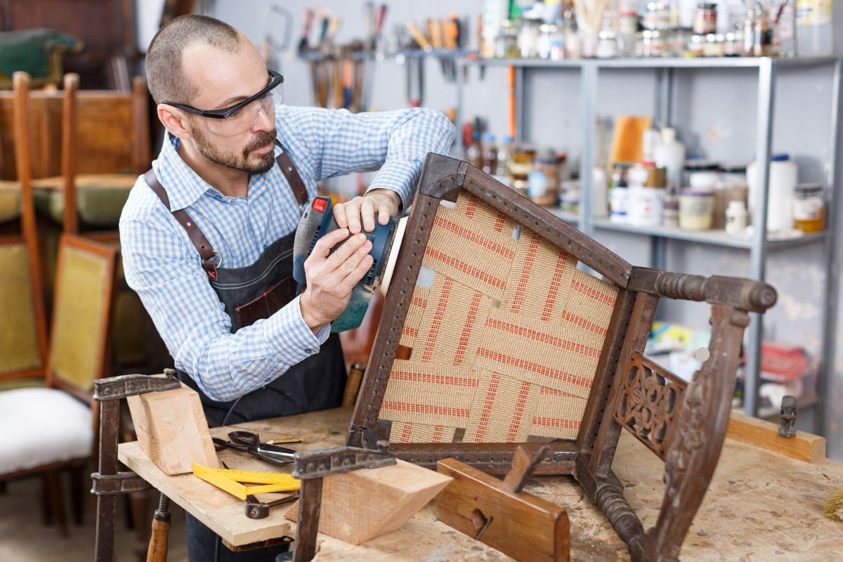 A man repairs an antique chair in a workshop, showcasing the widely accepted standards of antique furniture restoration.