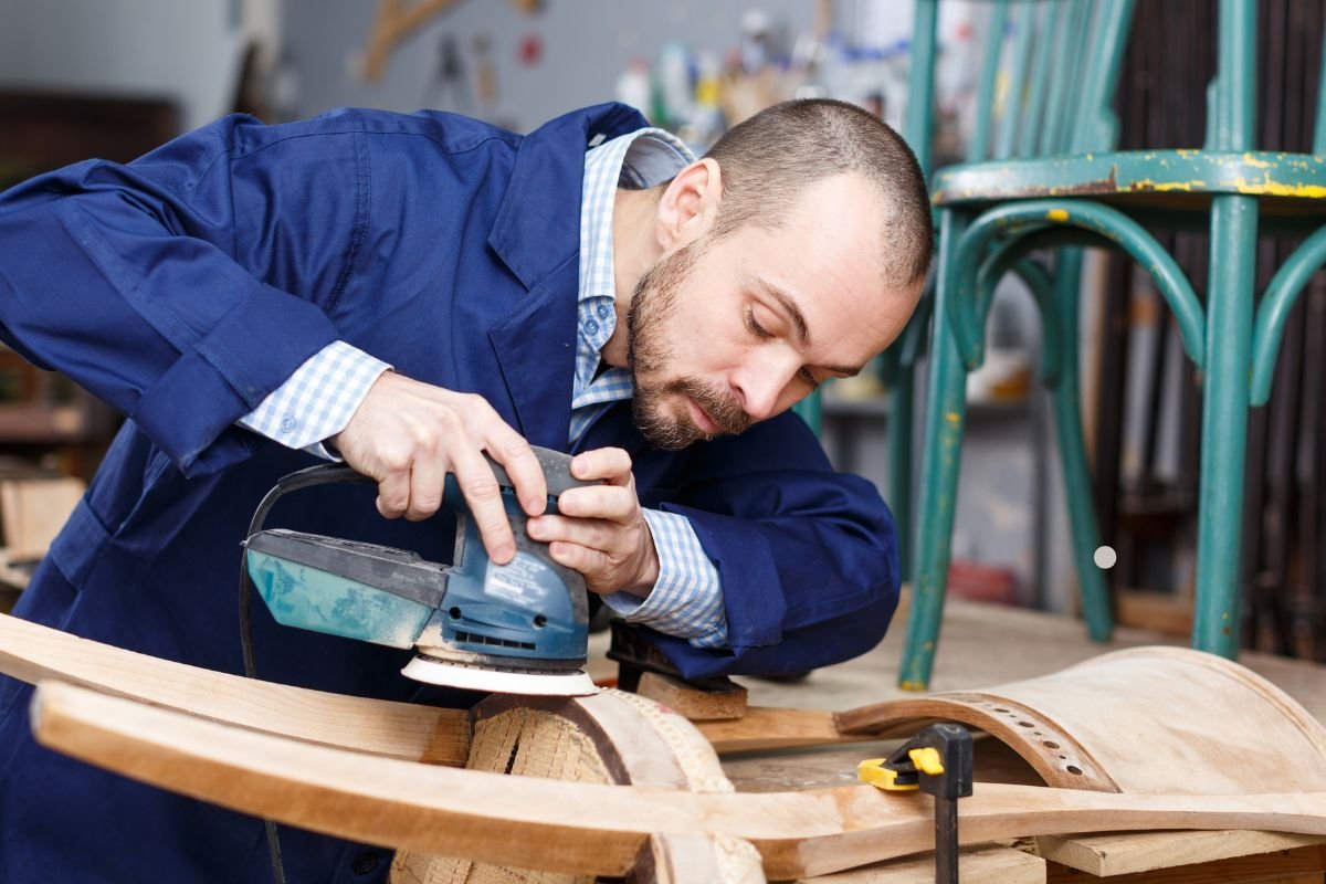 A man using a sander on wood, showcasing the craftsmanship of antique restoration and its historical significance. 